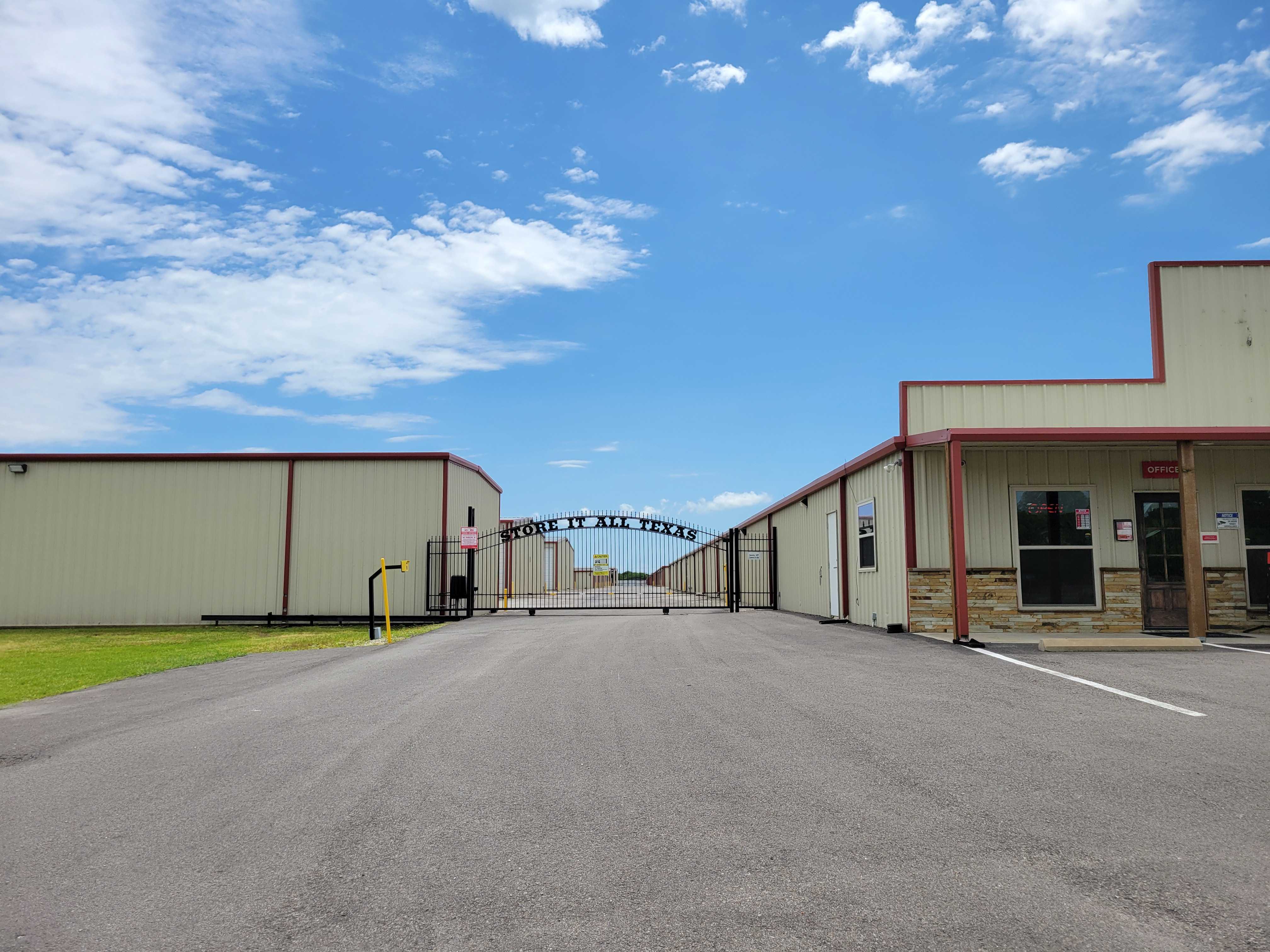 Secure gated entrance and office of Caddo Mills Climate Storage facility under a clear blue Texas sky